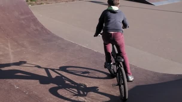 Un niño está montando trucos de ciclismo BMX en un parque de skate en un día soleado. Super cámara lenta — Vídeos de Stock