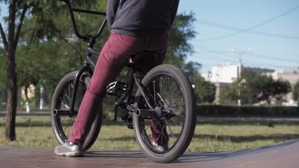 Un niño está montando trucos de ciclismo BMX en un parque de skate en un día soleado. Super cámara lenta — Vídeos de Stock