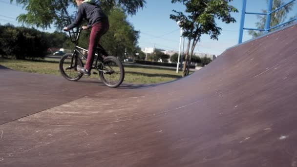 A boy is riding BMX cycling tricks in a skateboard park on a sunny day. Super Slow Motion — Stock Video
