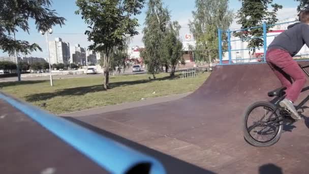 A boy is riding BMX cycling tricks in a skateboard park on a sunny day. Super Slow Motion — Stock Video