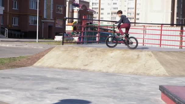 一个男孩在一个阳光明媚的日子, 在滑板公园里骑着小轮自行车的把戏。超慢动作 — 图库视频影像