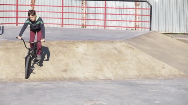 A boy is riding BMX cycling tricks in a skateboard park on a sunny day. Super Slow Motion — Stock Video