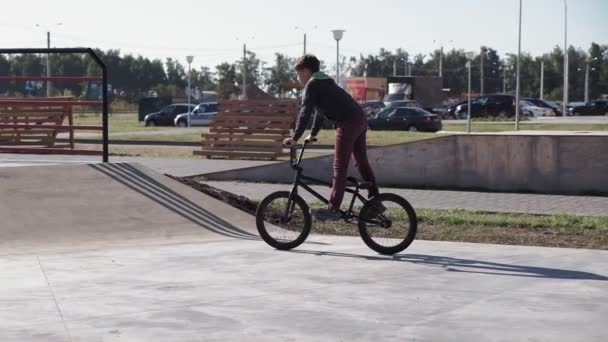 一个男孩在一个阳光明媚的日子, 在滑板公园里骑着小轮自行车的把戏。超慢动作 — 图库视频影像