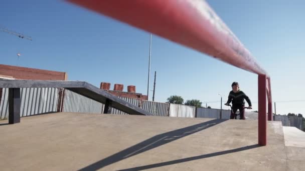 A boy is riding BMX cycling tricks in a skateboard park on a sunny day. Super Slow Motion — Stock Video