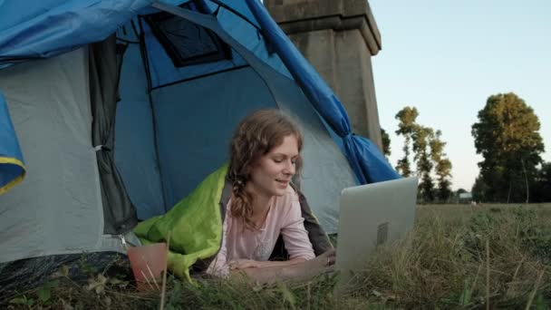 Mladá žena, pracující za notebook v turistické stanu nedaleko starého mostu — Stock video