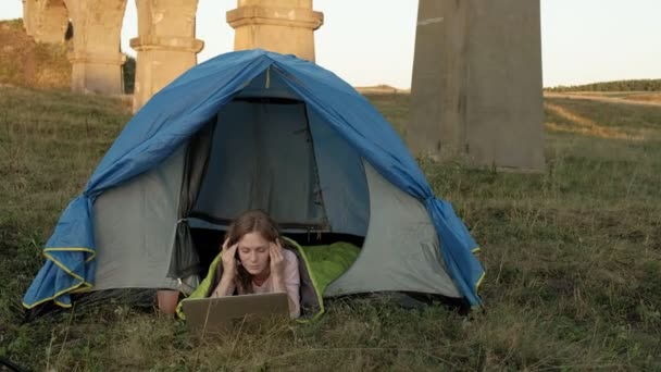 Jovem mulher trabalhando atrás de um laptop em uma tenda turística perto da ponte velha — Vídeo de Stock