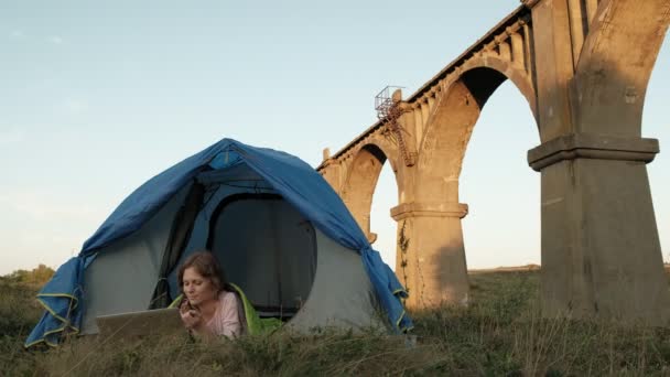 Jeune femme travaillant derrière un ordinateur portable dans une tente touristique près du vieux pont — Video