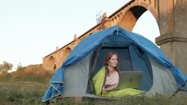 Jonge vrouw werken achter een laptop in een toeristische tent in de buurt van de oude brug — Stockvideo