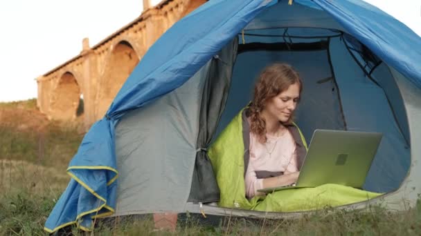 Fiatal nő dolgozik mögött egy laptop, egy turisztikai sátorban, közel a régi hídhoz — Stock videók