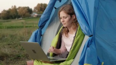 Bir dizüstü bilgisayar bir turist çadırda arkasında çalışan genç kadın