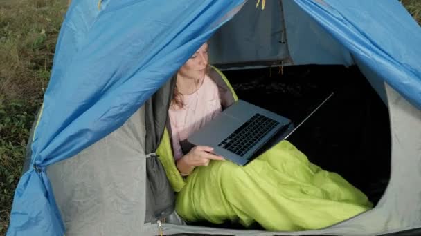 Mujer joven trabajando detrás de un portátil en una tienda de campaña turística — Vídeos de Stock