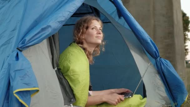 Mladá žena, pracující za notebook v turistické stanu nedaleko starého mostu — Stock video