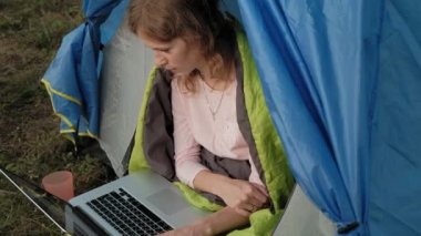 Bir dizüstü bilgisayar bir turist çadırda arkasında çalışan genç kadın