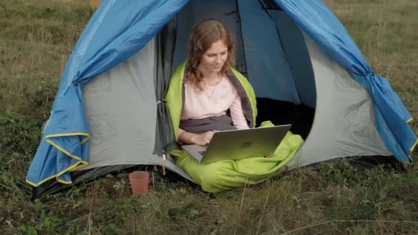 Молода жінка працює за ноутбуком у туристичному наметі — стокове відео