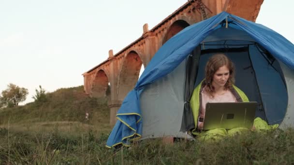Jonge vrouw werken achter een laptop in een toeristische tent in de buurt van de oude brug — Stockvideo