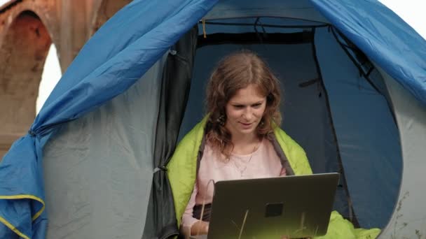 Ung kvinna som arbetar bakom en laptop i en turist tält nära den gamla bron — Stockvideo