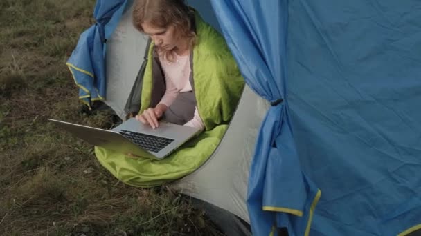 Junge Frau arbeitet hinter einem Laptop in einem Touristenzelt — Stockvideo