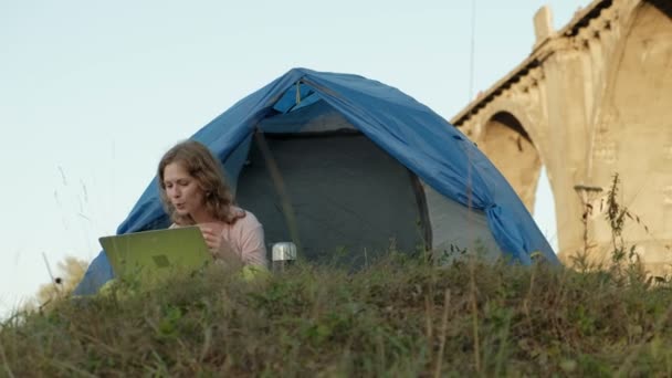 Jonge vrouw werken achter een laptop in een toeristische tent in de buurt van de oude brug — Stockvideo