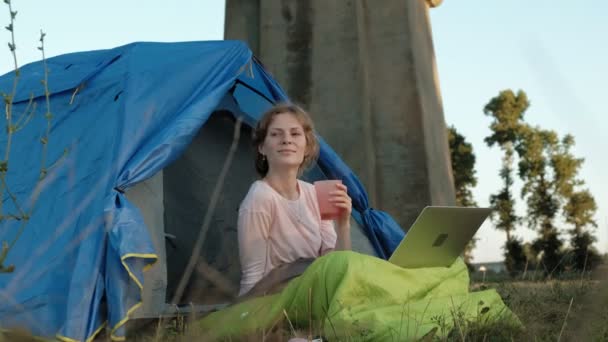 Молодая женщина, работающая за ноутбуком в туристической палатке возле старого моста — стоковое видео