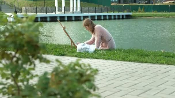 Una mujer bonita con el pelo rojo, pinta un cuadro sobre lienzo, que se encuentra en el caballete. La señora está en el aire libre cerca del lago del río, ella saca de la vida — Vídeos de Stock