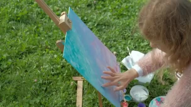 A pretty woman with red hair, paints a picture on canvas, which stands on the easel. The lady is in the open air near the lake of the river, she draws from life — Stock Video