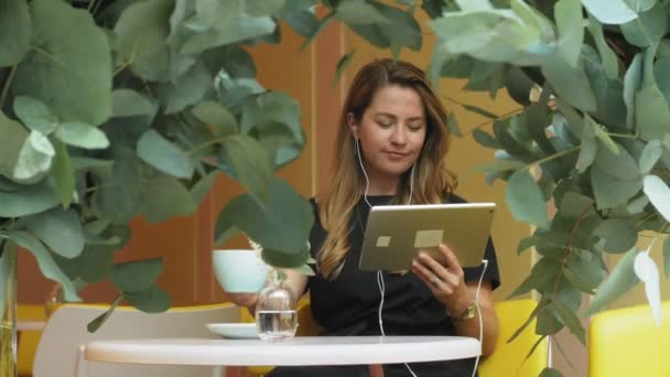 Femme d'affaires assise à une table dans un café buvant du café et travaillant sur une tablette — Video