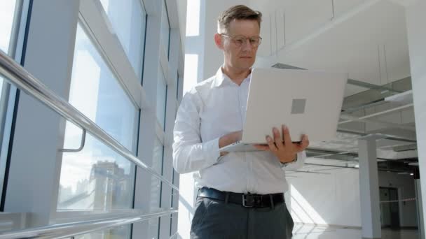 Uomo d'affari maturo a una finestra con un computer portatile — Video Stock