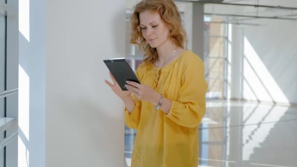 Jonge mooie zakenvrouw, bij het raam met een tablet — Stockvideo