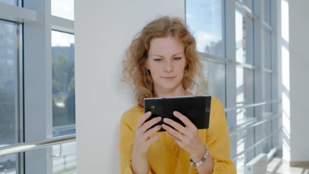 Jonge mooie zakenvrouw, bij het raam met een tablet — Stockvideo