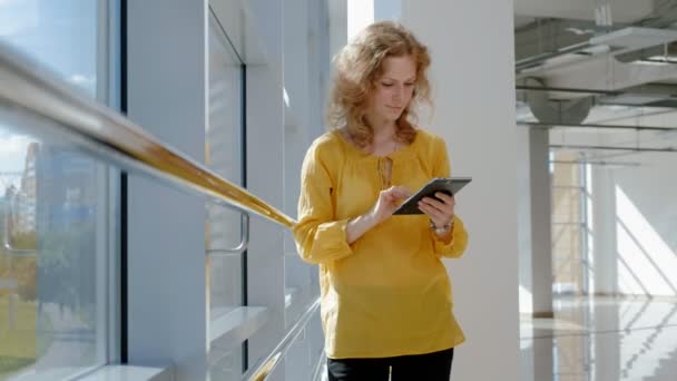 Junge schöne Geschäftsfrau, am Fenster mit einem Tablet — Stockvideo