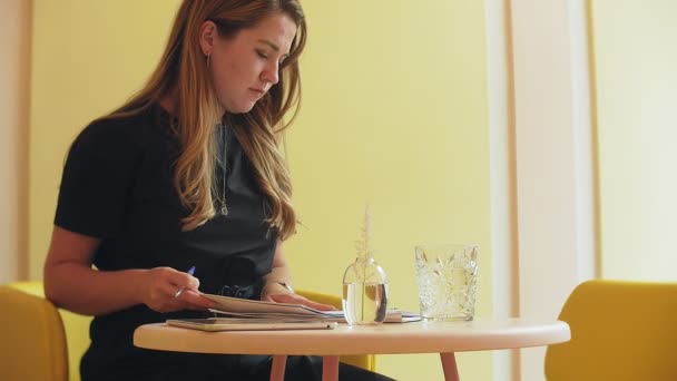 Business woman sitting at a table in a cafe drinking coffee and working on a tablet — Stock Video