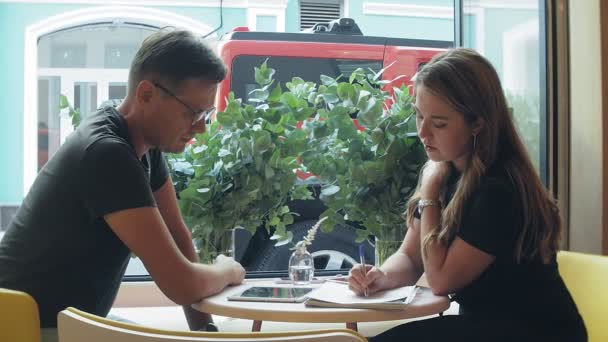 Eine Geschäftsfrau und ein Mann sitzen in der Pause mit ihrem Tablet in einem Café mit gelben Wänden und besprechen ein Projekt — Stockvideo