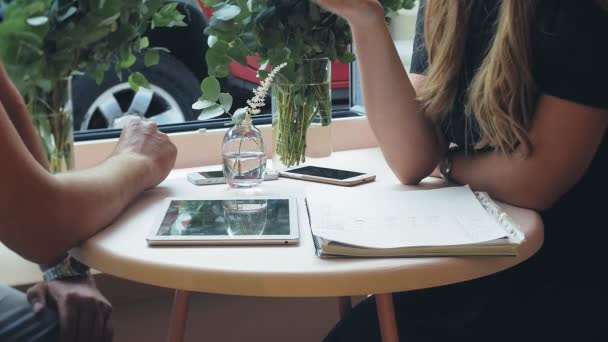 Деловая женщина и мужчина во время перерыва со своим планшетом сидят в кафе с жёлтыми стенами и обсуждают проект — стоковое видео