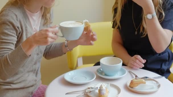 Dos mujeres sentadas en un restaurante cafetería comiendo pasteles eclair bebiendo café y riendo — Vídeos de Stock