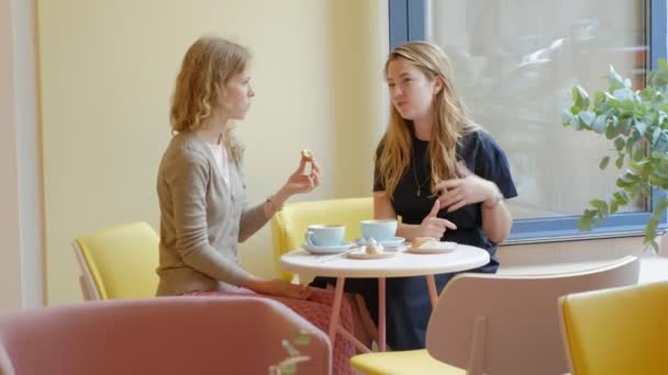 Dvě ženy sedící v restauraci café jíst koláče éclair pití kávy a směje se — Stock video