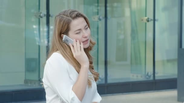 Joven mujer de negocios hablando está utilizando el teléfono inteligente en el centro de negocios del parque de la ciudad — Vídeo de stock