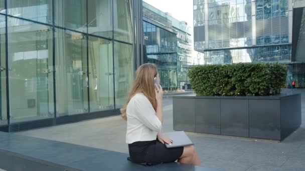 Joven mujer de negocios hablando está utilizando el teléfono inteligente en el centro de negocios del parque de la ciudad — Vídeos de Stock