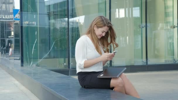 Joven mujer de negocios hablando está utilizando el teléfono inteligente en el centro de negocios del parque de la ciudad — Vídeos de Stock