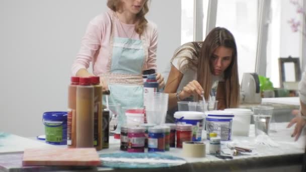 Жінки в художній студії змішують фарби і малюють на полотні в техніці рідинного мистецтва — стокове відео