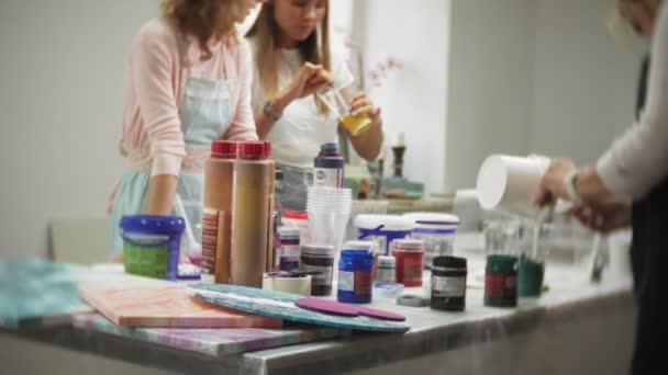 Women in an art studio mix paints and draw on canvas in fluid art technique — Stock Video