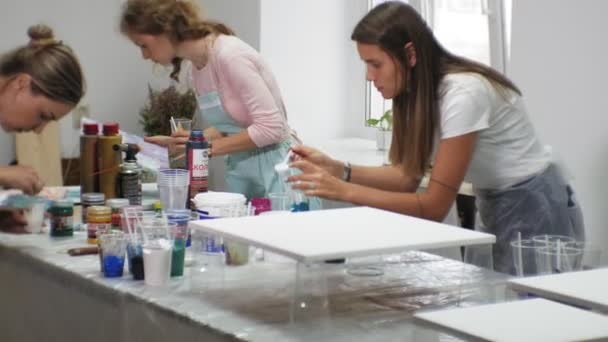 Mulheres em um estúdio de arte misturar tintas e desenhar sobre tela em técnica de arte fluida — Vídeo de Stock