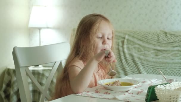 Щаслива красива дівчина їсть кашу на сніданок і розважається на білій кухні вдома — стокове відео