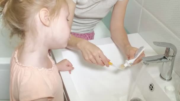 Moeder borstels zachtjes de tanden van haar geliefde dochter een klein meisje met haar moeder zacht reinigt tanden na het eten. — Stockvideo