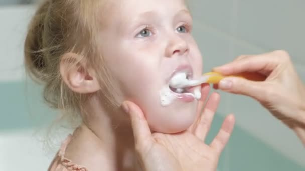 Maman brosse doucement les dents de sa fille bien-aimée Une petite fille avec sa mère nettoie doucement les dents après avoir mangé . — Video