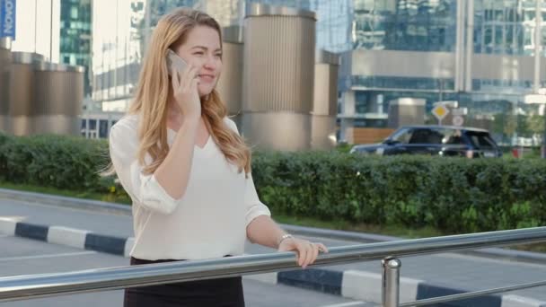 Joven mujer de negocios hablando está utilizando el teléfono inteligente en el centro de negocios del parque de la ciudad — Vídeos de Stock