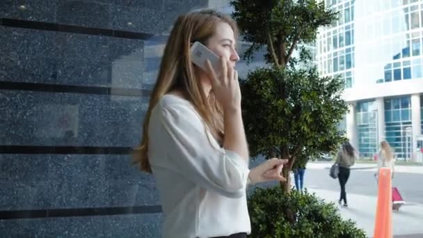 Νεαρή γυναίκα μιλάμε χρησιμοποιώντας το smartphone σε επιχειρηματικό πάρκο κέντρο — Αρχείο Βίντεο