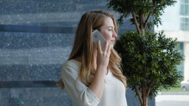 Joven mujer de negocios hablando está utilizando el teléfono inteligente en el centro de negocios del parque de la ciudad — Vídeos de Stock