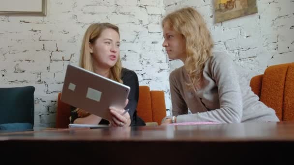 Två företagskvinnor med en pekplatta på kontoret är upptagna med att diskutera frågor — Stockvideo
