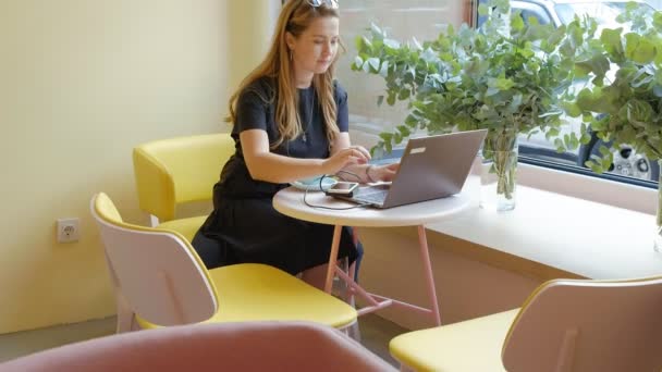 Деловая женщина сидит за столом в кафе, пьет кофе и работает на ноутбуке — стоковое видео