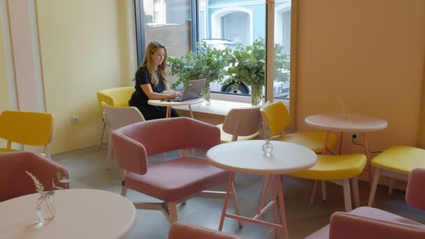 Mujer de negocios sentada en una mesa en un café tomando café y trabajando en un portátil — Vídeos de Stock